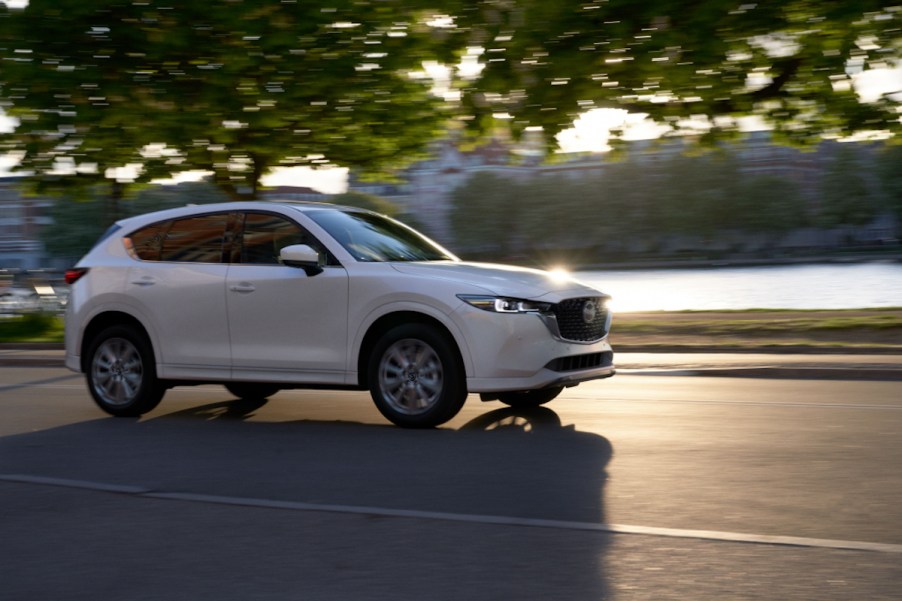 A white 2022 Mazda CX-5 2.5 Turbo Signature traveling on a road past a a waterway and buildings