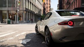 A 2022 Mazda MX-5 Miata coupe roadster model with a white paint color option stopped in a lane at a traffic light stop