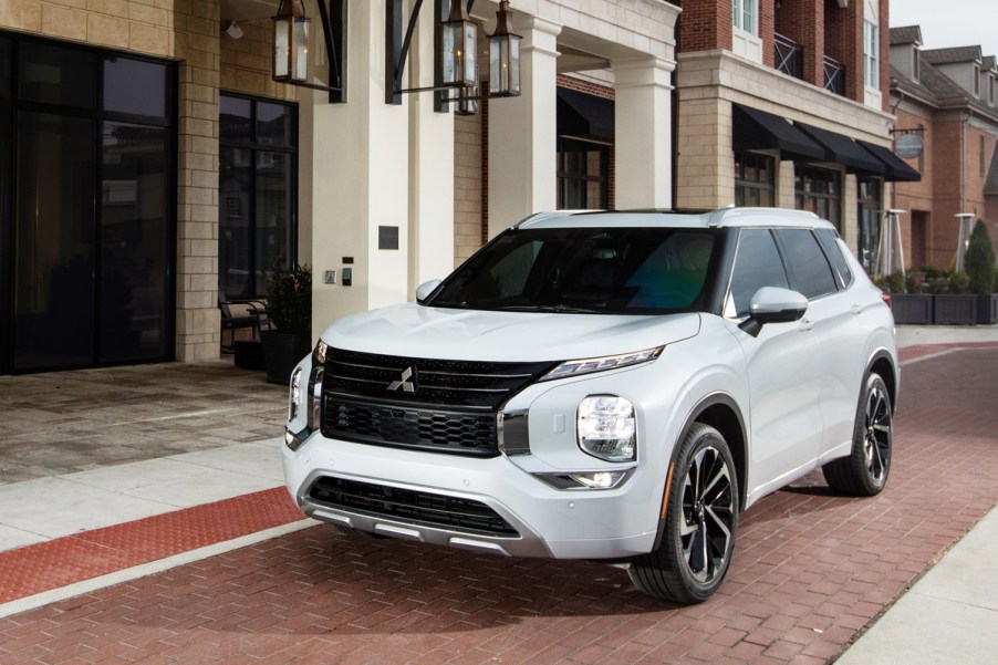 A white 2022 Mitsubishi Outlander compact crossover SUV parked on a brick road outside a brick storefront