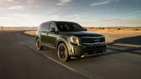 A dark colored 2022 Kia Telluride driving on a quiet road.