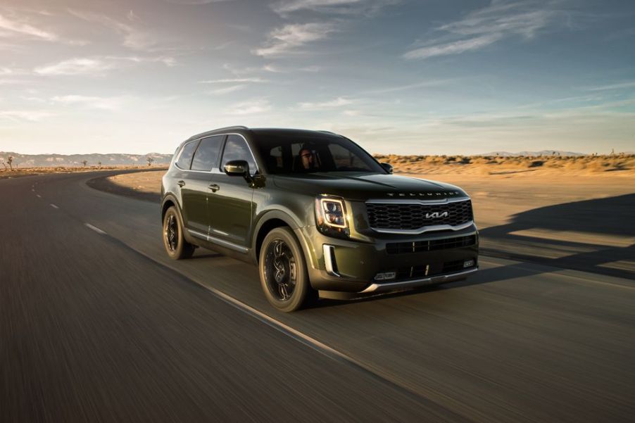 A dark colored 2022 Kia Telluride driving on a quiet road.