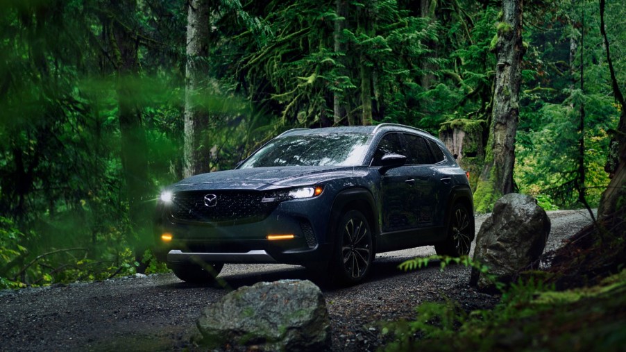 A dark blue 2023 Mazda CX-50 driving through the forest.