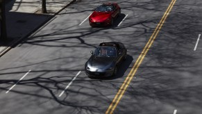 A gray 2022 Mazda MX-5 Miata RF and a red 2022 Mazda MX-5 Miata convertible drive down a city street