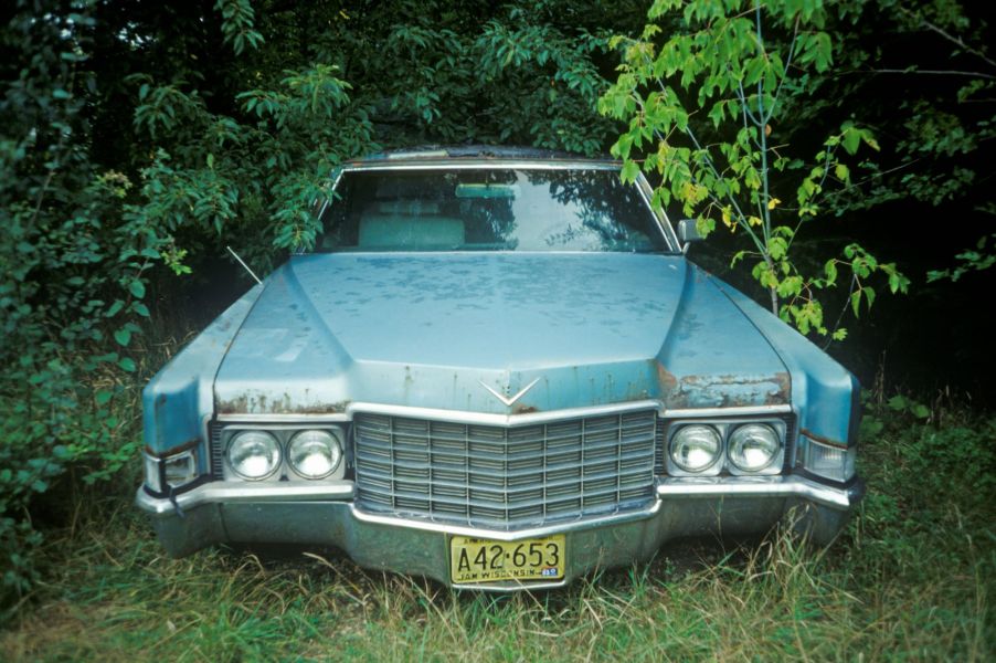 A blue abandoned car in the woods.