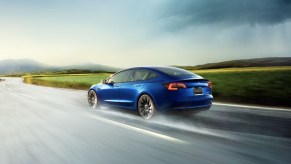 Blue 2022 Tesla Model 3 driving on a wet road, highlighting 2022 EVs that make an impact on climate change