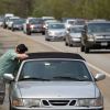 A silver with a lack top breaks down on a highway with a person leaning against the car.