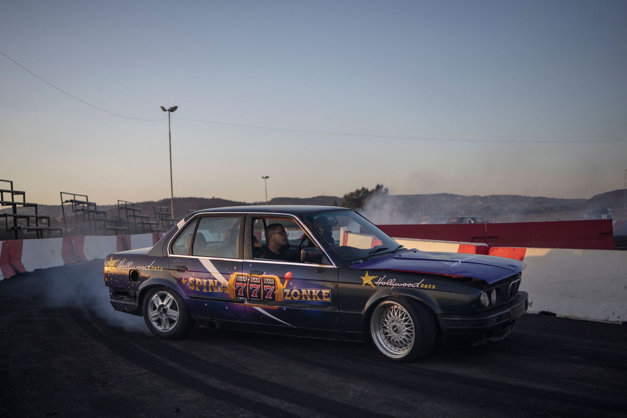 A blue car with decals drifting on a race track. 