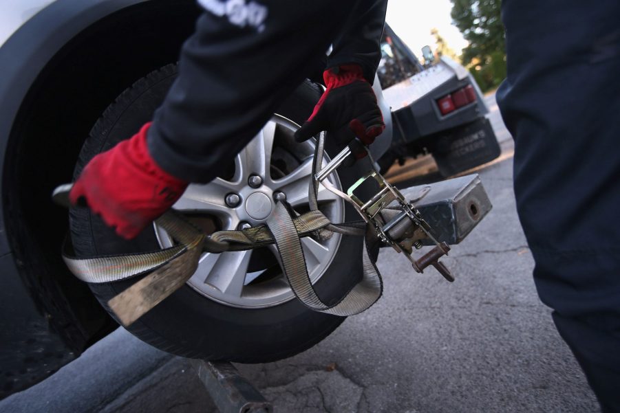 A car repossession occurring by strapping straps to the tires.