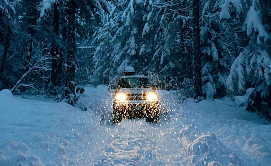 Car warms up with headlights on a snowy path in the forest