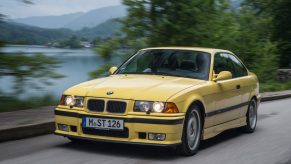 A yellow E36 BMW M3 Coupe drives around a mountain lake