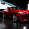 A red Mazda 6 parked in an indoor area with a screen in the background showing a highway with another Mazda 6 driving on it.