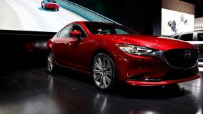 A red Mazda 6 parked in an indoor area with a screen in the background showing a highway with another Mazda 6 driving on it.