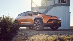 Orange 2023 Fisker Ocean, one of the cheapest electric crossover SUVs available to buy in 2022, parked next to a lifeguard tower