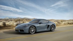 A blue/gray Porsche 718 Cayman driving on a desert road