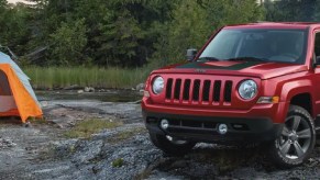 A red Jeep Patriot parked next to a tent.