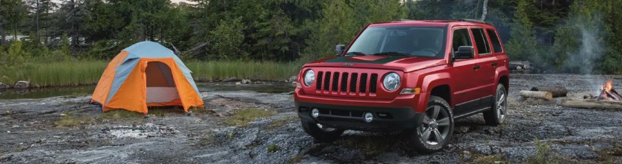 A red Jeep Patriot parked next to a tent.