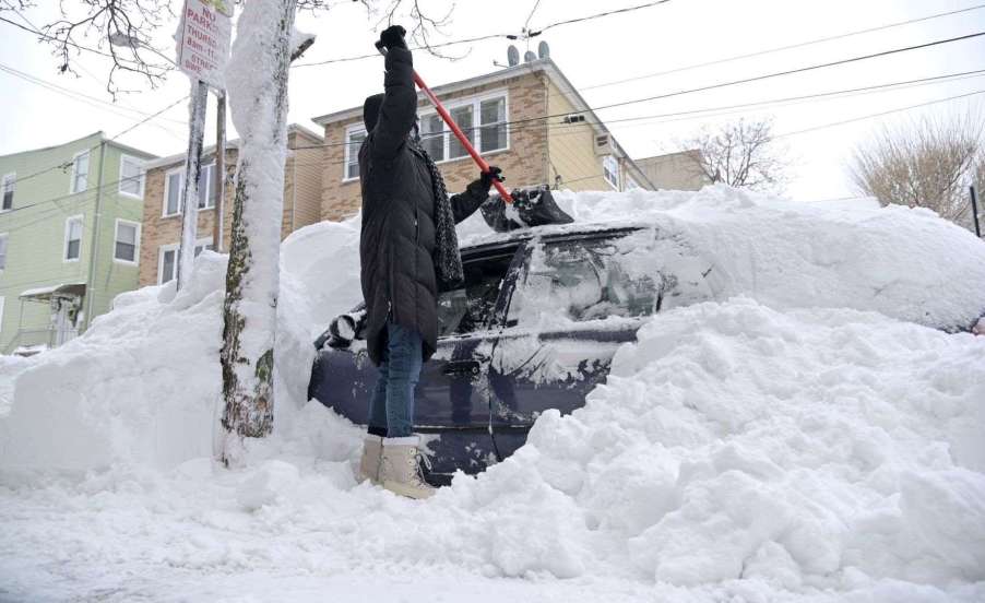 Person shoveling snow off a car, highlighting story about an electric vehicle warming up a cabin in cold weather