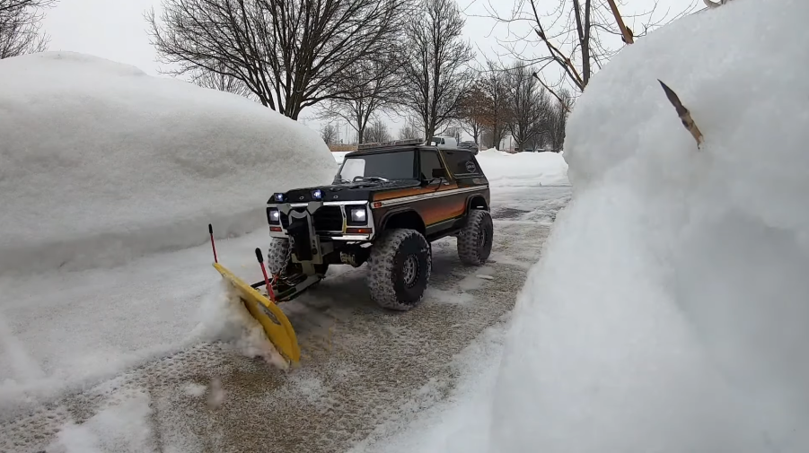 An RC Ford Bronco with a snow plow attachment clears a driveway of snow in the winter