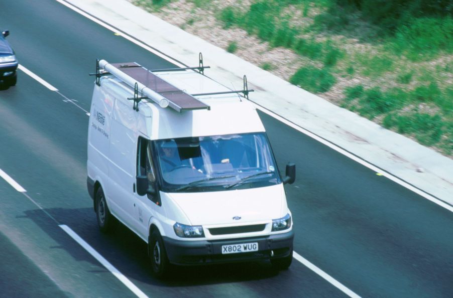 A white van with a roof rack on top driving down the highway.