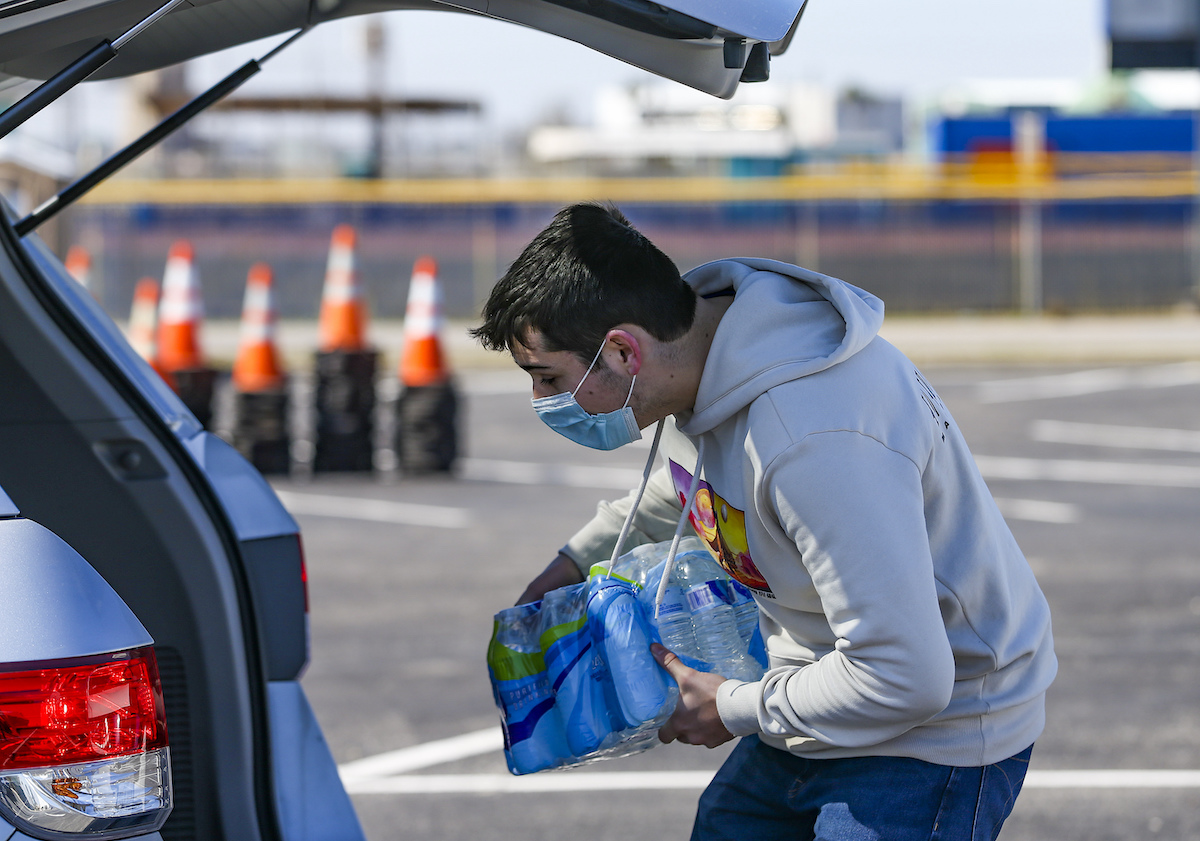 A man places water bottles into the back of a car in winter 2021 in Galveston, Texas