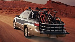 The rear 3/4 view of a green-and-tan 2005 Subaru Baja driving through the desert