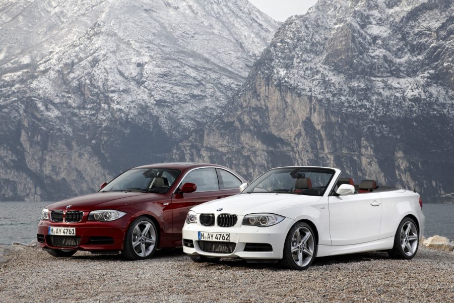 A red 2012 E82 BMW 135i Coupe next to a white 2012 E88 BMW 135i Convertible by a mountain lake