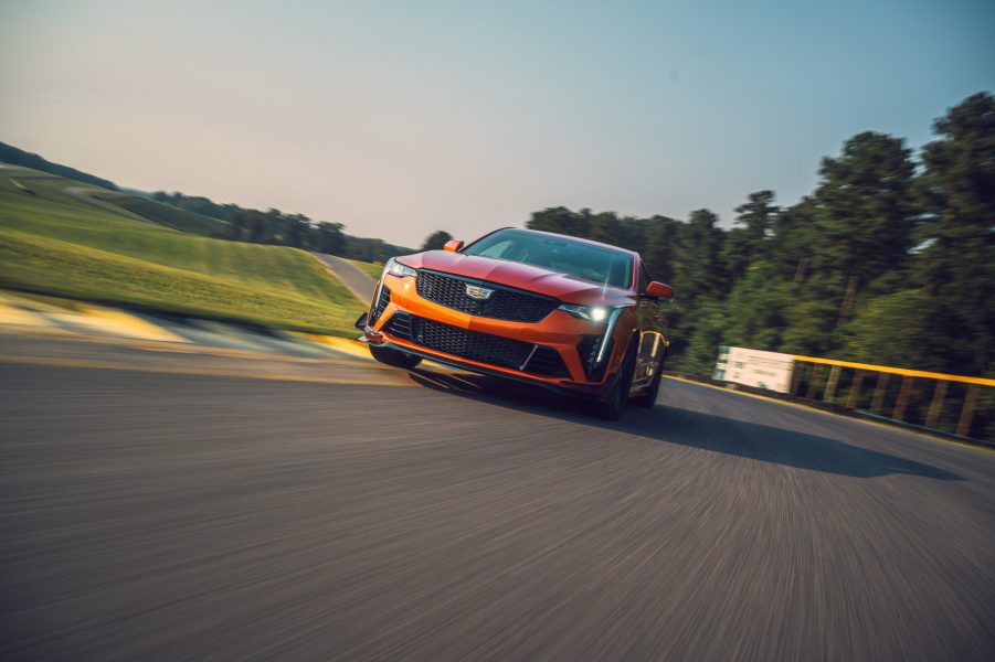 A front view of an orange 2022 Cadillac CT4-V Blackwing cornering on a race track with trees in the background