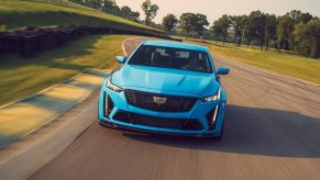 A front view of a blue 2022 Cadillac CT5-V Blackwing cornering on a race track with trees in the background.