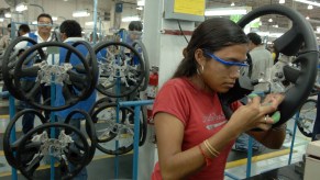 A woman in a Mexican assembly line upholstering a black steering wheel for a Chevy Silverado.