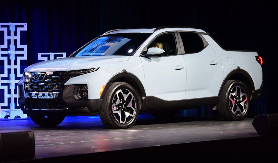 A white 2022 Hyundai Santa Cruz in front of a black background with a lite blue pattern.