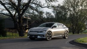 A silver 2022 Kia EV6 surrounded by trees with a building in the background on a blacktop road.