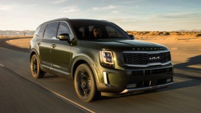 A green 2022 Kia Telluride is driving on the road.