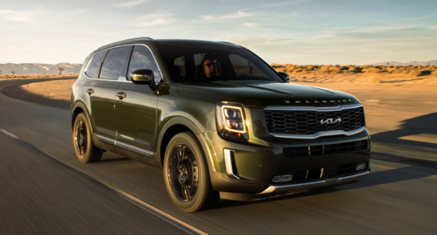 A green 2022 Kia Telluride is driving on the road.