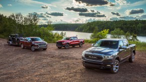 Three 2022 Ram 1500 pickup trucks parked on a dirt road in front of a farm.