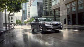 A 2022 Subaru Legacy Limited compact sedan with a Magnetite Gray Metallic paint color option driving through an urban city