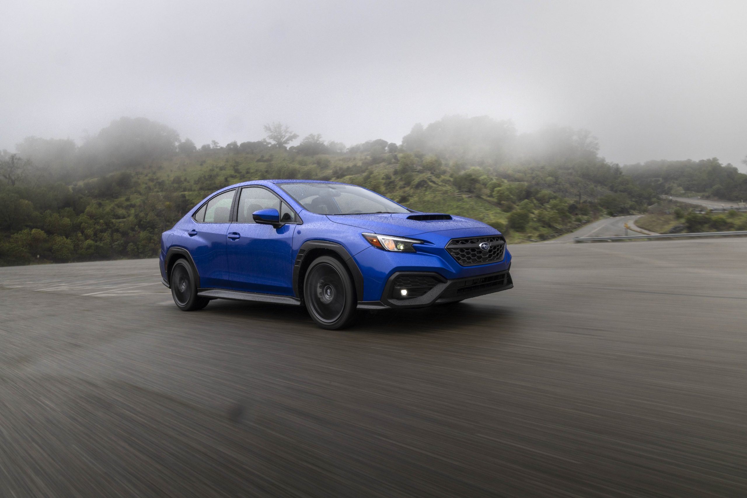 A blue 2022 Subaru WRX shot from the 3/4 angle on a rainy highway