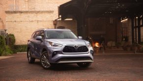 Promo shot of a blue 2022 Toyota Highlander Platinum crossover SUV parked in front of a white brick building.