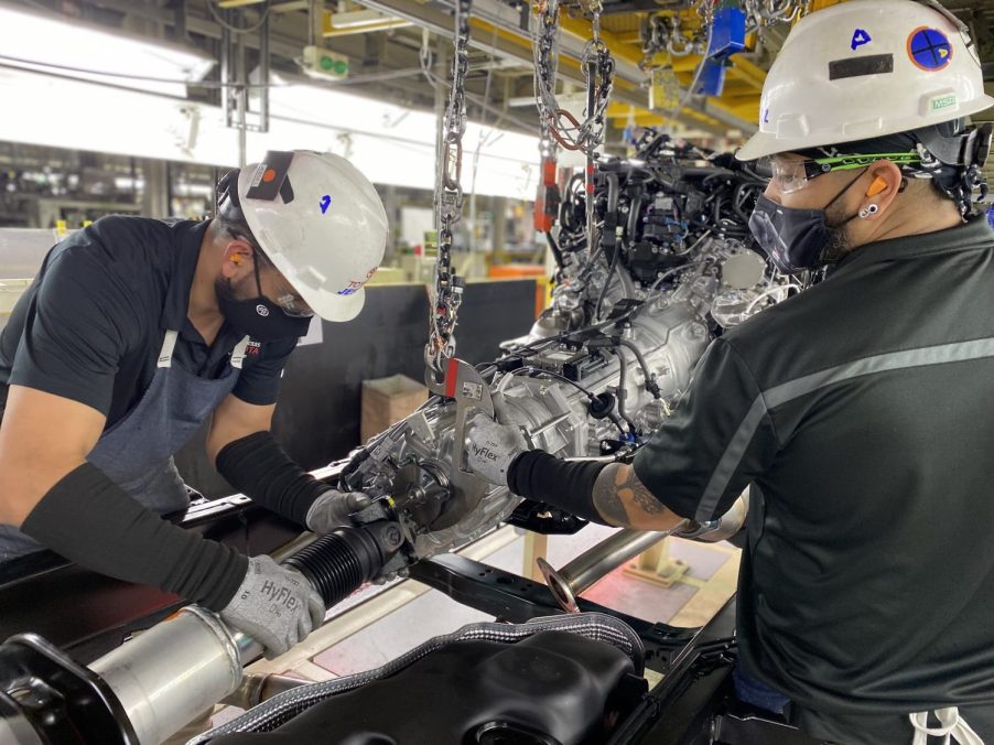 Two factory workers attaching a driveshaft to the transmission of a Toyota Tundra.