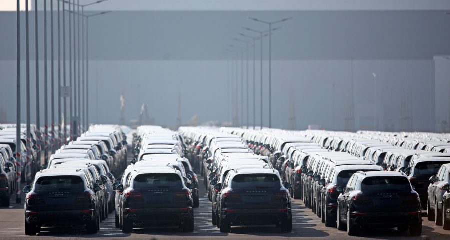 A large number of dark-colored Porsche Cayenne SUVs gathered in a parking lot for emissions-related recall work