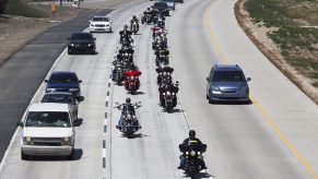 A line of motorcycle riders on the highway surrounded by cars