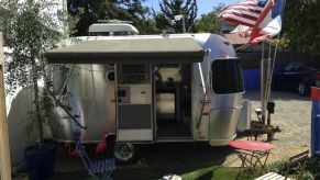 An Airstream Bambi parked outdoors with a rock path, American flag, and small table and chair.