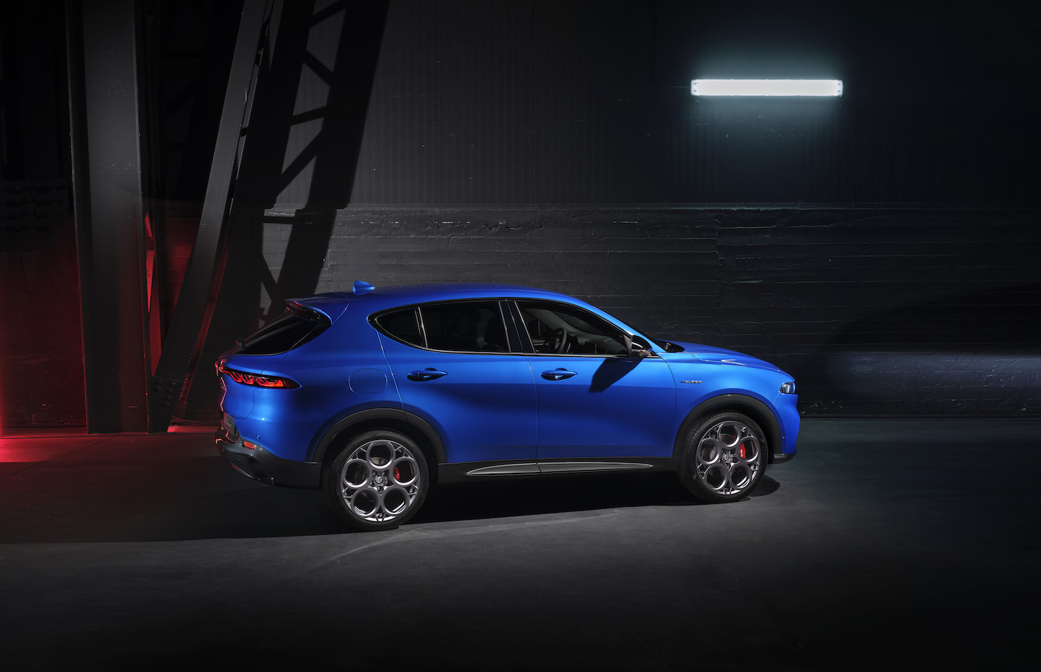 Promo shot of a blue Alfa Romeo Tonale or Dodge Hornet crossover SUV in front of a gray brick wall.