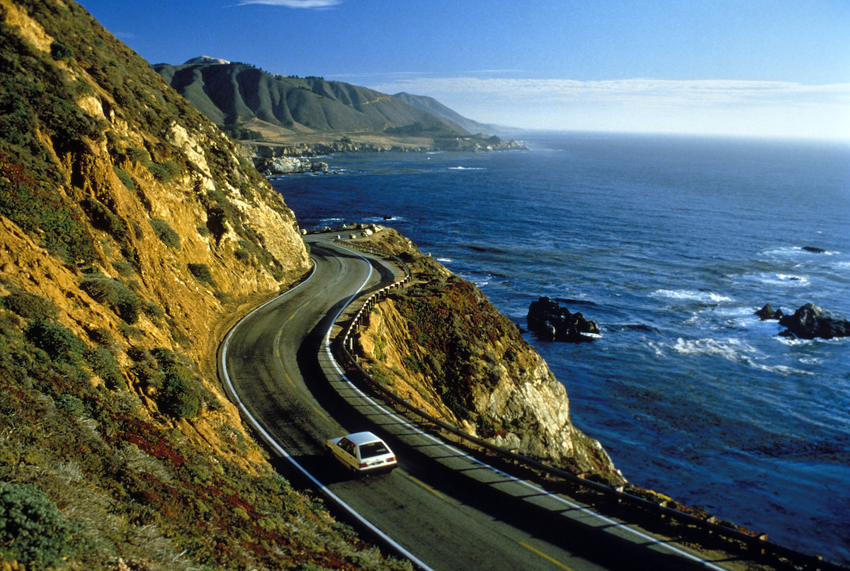 A white car drives near cliffs in Big Sur along California's Pacific coast