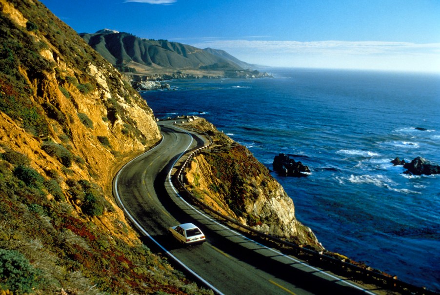 A white car drives near cliffs in Big Sur along California's Pacific coast