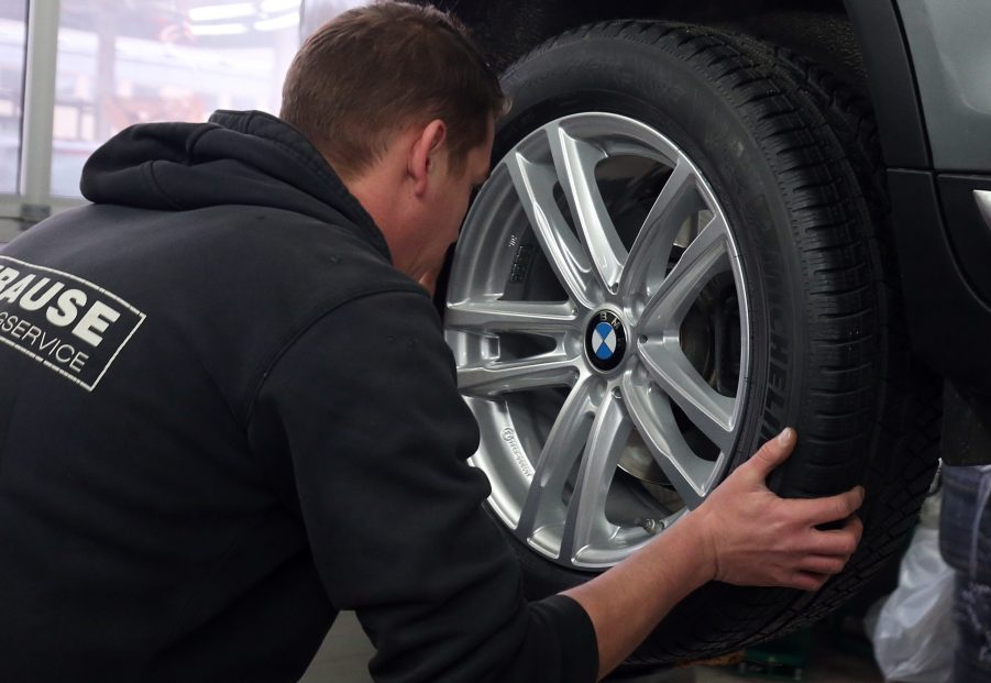 A man removes a car's wheel to inspect its wheel bearing