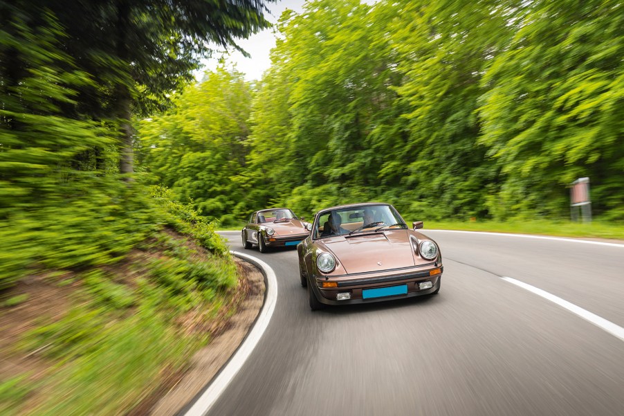 A pair of vintage 1970s Porsche sports cars, including a 1975 930 Turbo and a 1974 2.7 Carrera MFI, driving in the hills outside Vienna