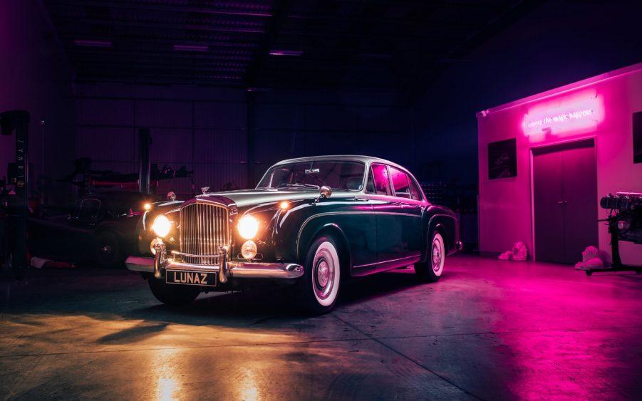 A blue-and-silver Lunaz classic Bentley Continental Flying Spur electric conversion by a garage