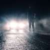 Man standing in front of a car with the high beam headlights activated