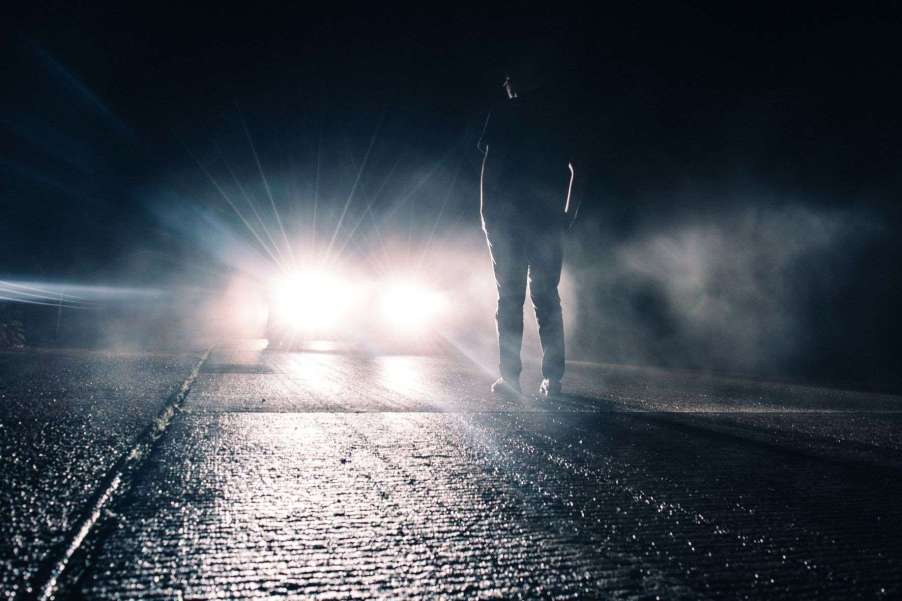 Man standing in front of a car with the high beam headlights activated