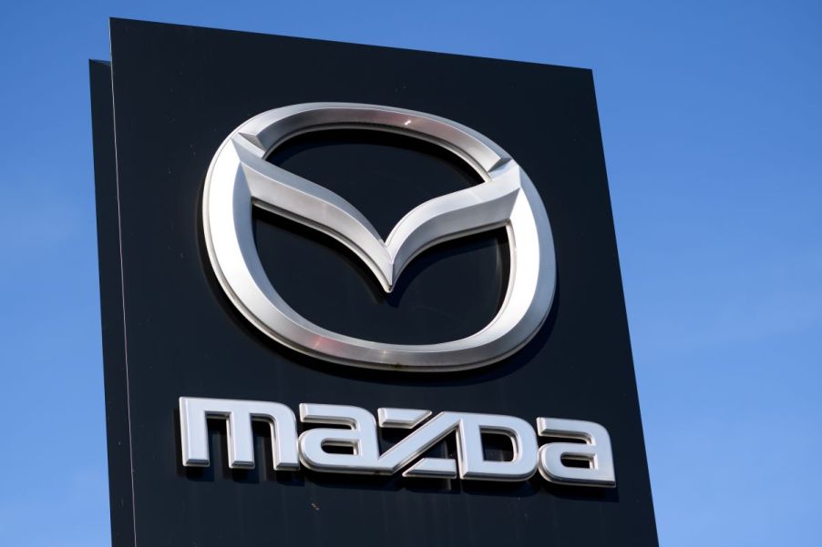 A black Mazda sign in front of a blue clear sky with the Mazda logo in silver on it.